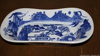 Elongated blue and white ceramic plate/bowl showing full scenic landscape design including mountains, houses, trees and bridge.
