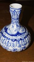 Full view of the vase showing the detailed blue floral and leaf patterns on a white ceramic surface. The vase has a bulbous base and a slim neck.