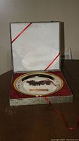 Bronze chariot and horses sculpture mounted on a decorative silver-toned plate inside an open box with red velvet lining.