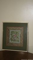 Full view of the framed tapestry showing the overall condition and presentation of the piece on a wall above furniture.