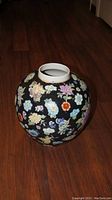 Side view of a hand painted Asian jar showing black background with multicolored floral designs.