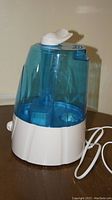 Side view showing humidifier with blue tank and white base on wooden table, power cord visible.