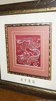 Full framed brocade textile featuring embroidered dragon motif and Chinese characters under glass.