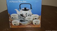 Box displaying 8-piece tea set including teapot and six cups