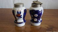 Front view of porcelain shaker and salter showing painted floral designs and cobalt blue areas with metal lids.