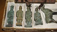 Close-up of five greenish patina Terracotta Warrior figurines in individual compartments of a fabric box.