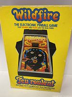 Front view of the vintage Wildfire pinball game box with bright yellow background and colorful game image.