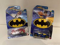 Two Hot Wheels DC Batman die-cast cars in original packaging, one blue with Batman images, one red with DC villains characters.