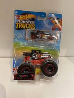 Two images of brand new Hot Wheels Monster Trucks Bone Shaker sets in original packaging. Each set has one monster truck and one smaller car with skull and flame designs.
