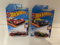 Two Hot Wheels Track Stars series cars in sealed packaging, one red and one blue.