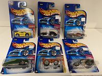 Six Hot Wheels cars in original packaging displayed on a white surface showing front angles and labels.