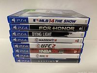 Side stacked view of 8 PS4 games showing titles on spine including MLB 14 The Show, For Honor, Dying Light, Madden 16, UFC 2, NBA 2K15, NHL 16, Destiny.