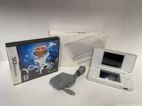 White Nintendo DS Lite handheld console open, with box and charger cable nearby