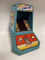 Side angle view showing Donkey Kong handheld arcade game in blue plastic casing with joystick, start button, and colorful game graphics.