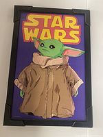 Framed 11x17 poster of Baby Yoda (Grogu) from Star Wars with purple background and 'STAR WARS' text at the top in yellow and red.