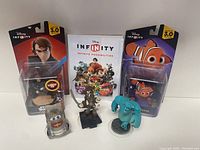 Lot items arranged showing face of Anakin Skywalker and Nemo figures in packaging, loose figures of Sulley, Tow Mater, and Sven, and the Disney Infinity guide booklet.
