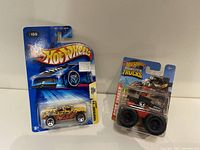 Photo of the two Hot Wheels die-cast vehicles in their original packaging, showing the leopard print Humvee and the black monster truck.
