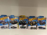 Photo showing full lot of five Hot Wheels vehicles in original packaging, various colors and models including purple, black, green, yellow, blue cars.