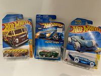 Three Hot Wheels cars in original packaging; Surf 'n School Bus, Asphalt Jungle Green car, and blue Torpedo dragster.