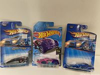 Lot of three Hot Wheels diecast cars in original packaging with blue backing cards and price stickers, showing overall packagings and cars inside.