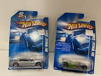 Front view of two Hot Wheels cars in original packaging, one silver and one green.