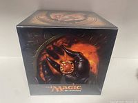 Front and top views of new Ultra Pro Magic The Gathering deck box with artwork of a black-gloved hand holding a red pendant against fiery background.