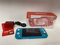 Overview of turquoise Switch Lite console, retail box, AC adapter, red game case with cartridge