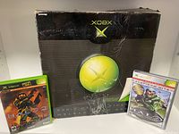 Front side of original Xbox box with two Xbox games (Halo 1 and Halo 2) in cases displayed beside it.