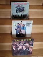 Front view of three Beatles vinyl LP records arranged on stairs, showing cover art of Beatles '65, Yesterday and Today, and a candid photo album cover.