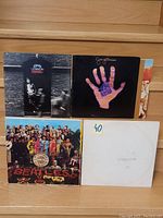 Front covers of four vinyl LP records showing John Lennon, Genesis, and two Beatles albums.