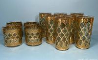 Angle view of the full set showing seven tall tumblers and four old fashioned glasses with gold and green intricate Valencia pattern