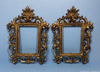 Two ornate antique Victorian metal photo frames with intricate leaf and scrollwork designs on a blue background.