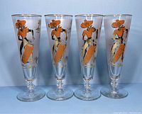 Front view of the four vintage Libbey Caribbean Calypso pilsner glasses showing dancing figure design in orange and gold on frosted glass.