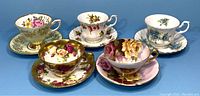 Overview of 5 teacups and saucers with varied floral patterns and gold trim