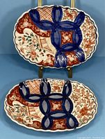 Pair of 19th century Japanese Imari oval porcelain plates showing decorative hand-painted floral and geometric patterns in blue, red, and green with scalloped edges.