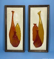 Pair of framed Mid-Century Modern 3D wall art pieces with abstract vase shapes in amber, red, and yellow on textured ivory backgrounds in wood frames.