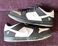 Side view of left and right sneaker stacked, showing black and white leather upper and pigeon embroidery on heel.