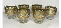 Six gold and green decorated footed rock glasses set in a row, showing all six items in the lot.