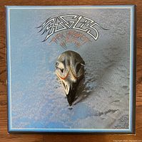 Front cover of The Eagles Greatest Hits vinyl LP showing silver-blue background with black eagle skull and stylized Eagles logo.