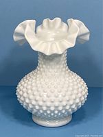 Front view of the white milk glass Fenton hobnail vase with prominent ruffled crimped rim on a blue background.