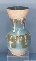 Front view of ceramic vase showing textured off-white upper and lower sections with olive green and light blue glaze with dripping effect in the middle.