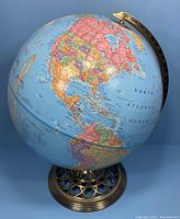 Front and center photo of the globe showing North and South America on the sphere, mounted on an ornate metal stand.