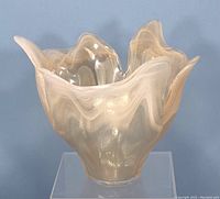 Front angled view of translucent Murano glass vase with petal-like ruffled edges and beige marble swirl pattern, displayed on a clear stand.