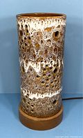 Front view of vintage ceramic cylindrical lamp showing cratered textured surface with white glaze and light brown color on teak circular base.