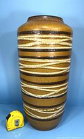 Front view of the large vintage floor vase with a yellow measuring tape beside it for scale.