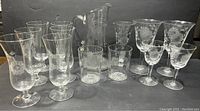 Full set display on a dark background showing all glasses, pitcher, and bud vase with etched corn flower pattern.