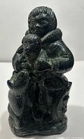 Front view of dark stone sculpture of Inuit man holding bear cub with a second bear at his side.