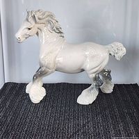 Full side view of the shiny white porcelain Shire horse figurine showing detailed mane, tail, and feathered hooves in cantering pose.