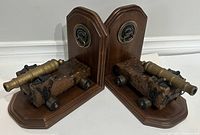 Pair of large wood and brass military-themed bookends with cannons mounted on wooden carriages, displayed side by side.