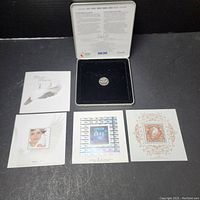 Collector coin displayed inside black lined tin case lid with text inside the lid.